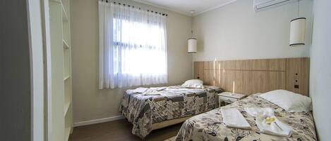 A hotel room with two beds, a window with curtains, a ceiling fan, an air conditioning unit, and a wooden headboard.