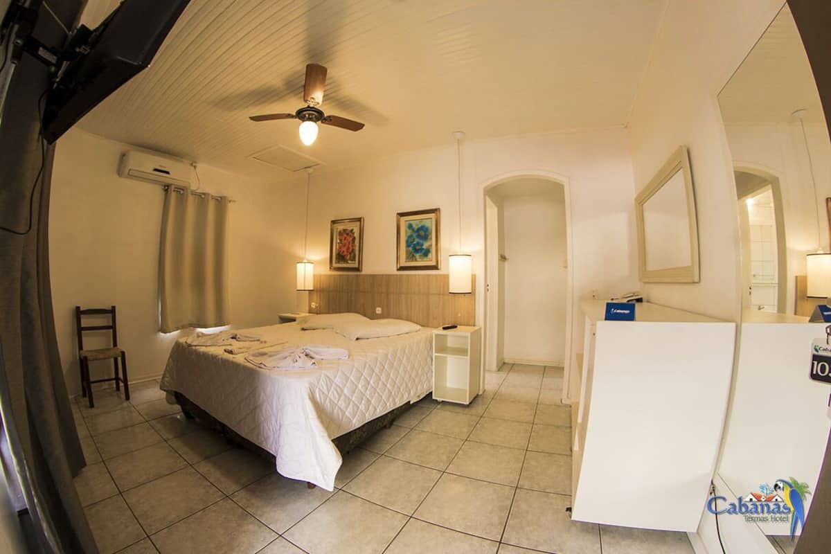A hotel room with a bed, a desk, a chair, a ceiling fan, and a mirror.