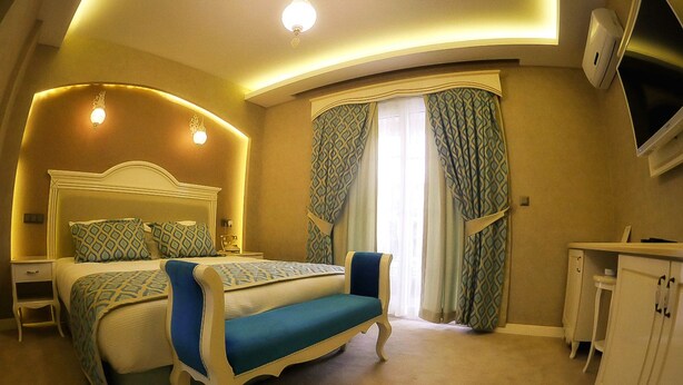 A bedroom with a bed, bedside tables, a desk, a chair, and a TV. - Hatunca Otel & Restaurant (Amasya)
