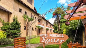 En træbænk, et skilt for Hotel Pousada Kaster, og en bygning med facade af mursten.