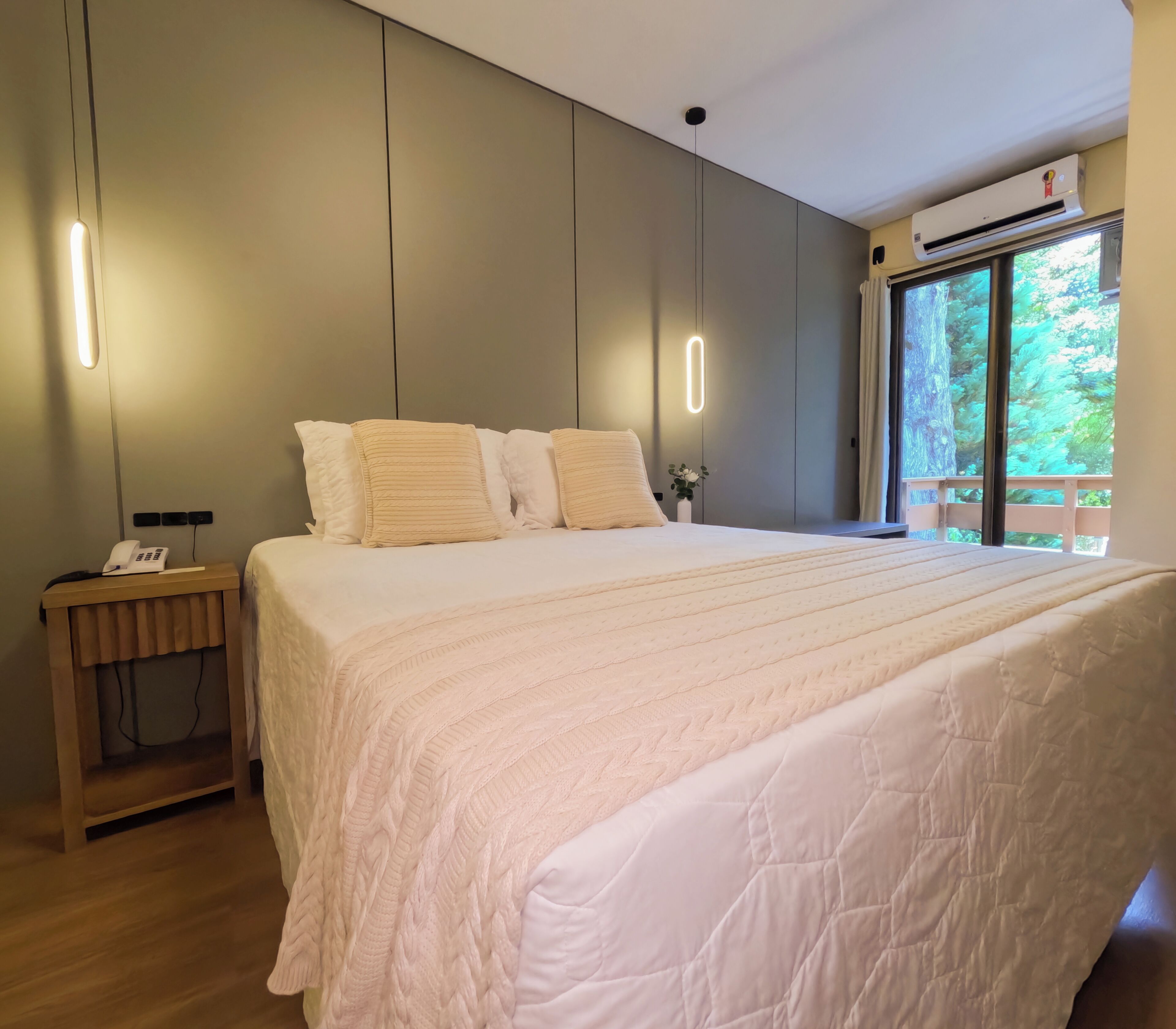 A bedroom with a large bed, bedside tables, a phone, and an air conditioning unit.