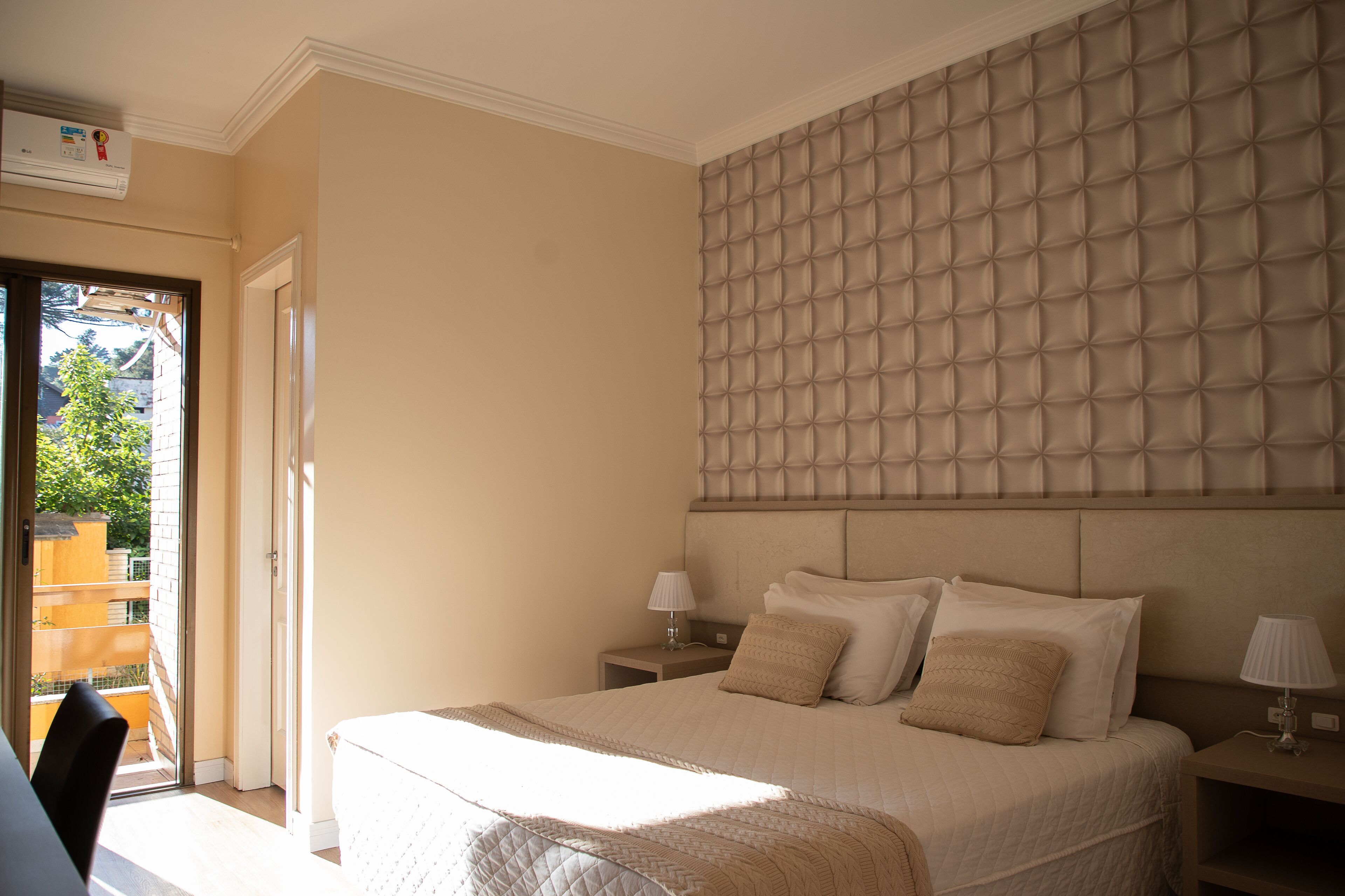 A bedroom with a large bed, a padded headboard, two bedside tables with lamps, and a sliding glass door leading to an outdoor area.
