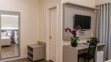 A hotel room with a bed, a desk, a chair, a TV, and a small cabinet.