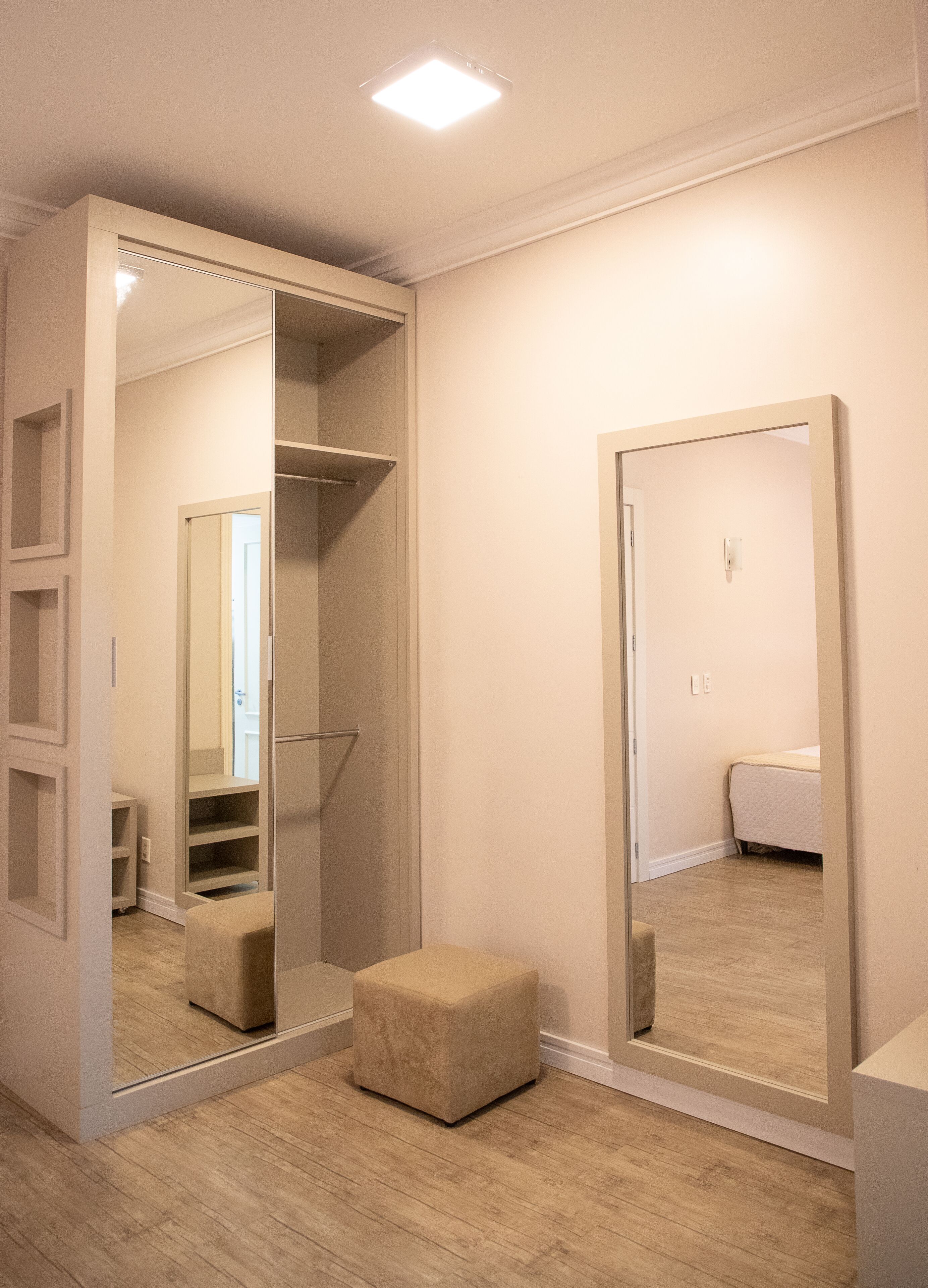A room with a large mirror, a walk-in closet, and a small ottoman.