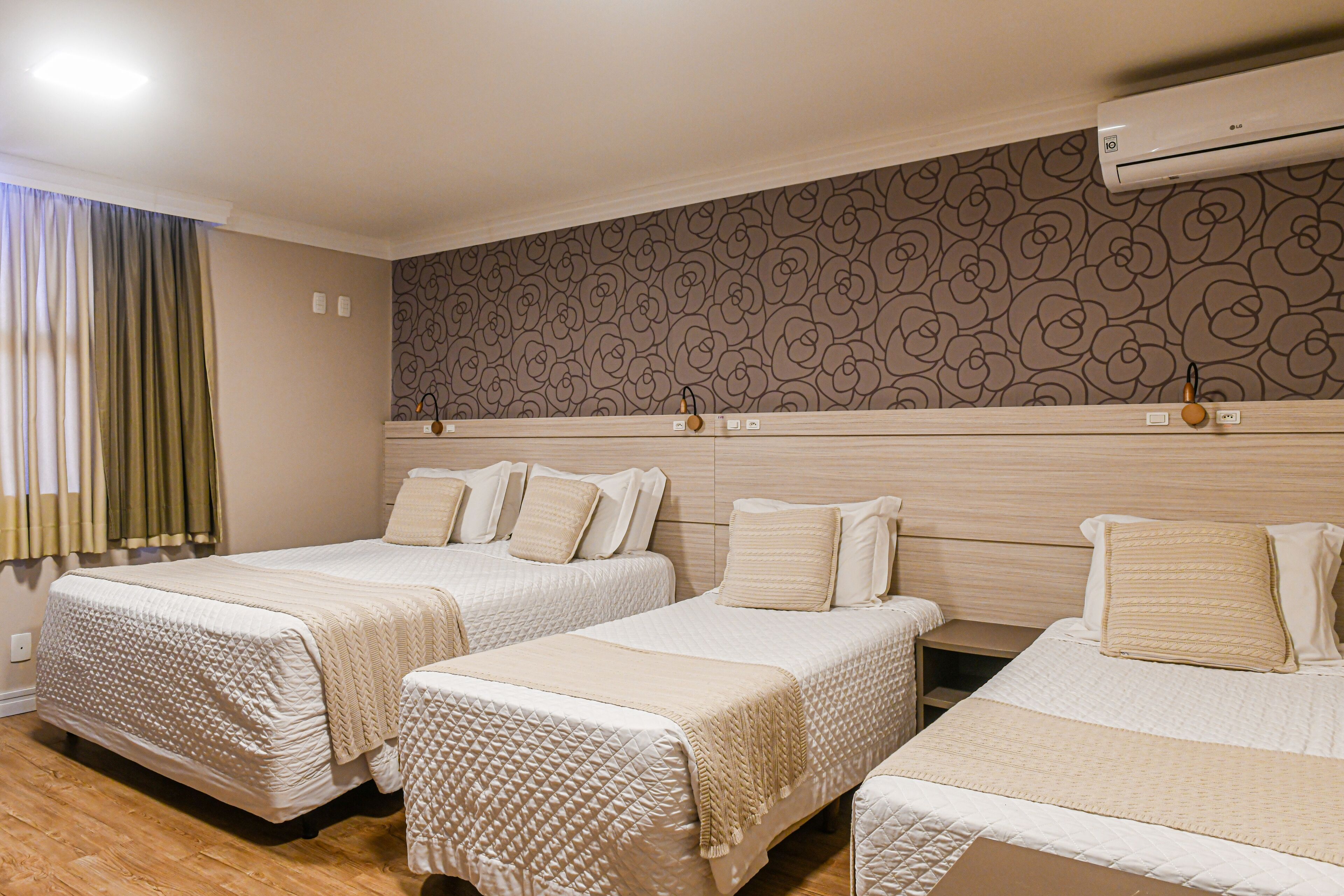 Une chambre d’hôtel avec deux lits, une tête de lit en bois, un papier peint à motifs et un appareil de climatisation.