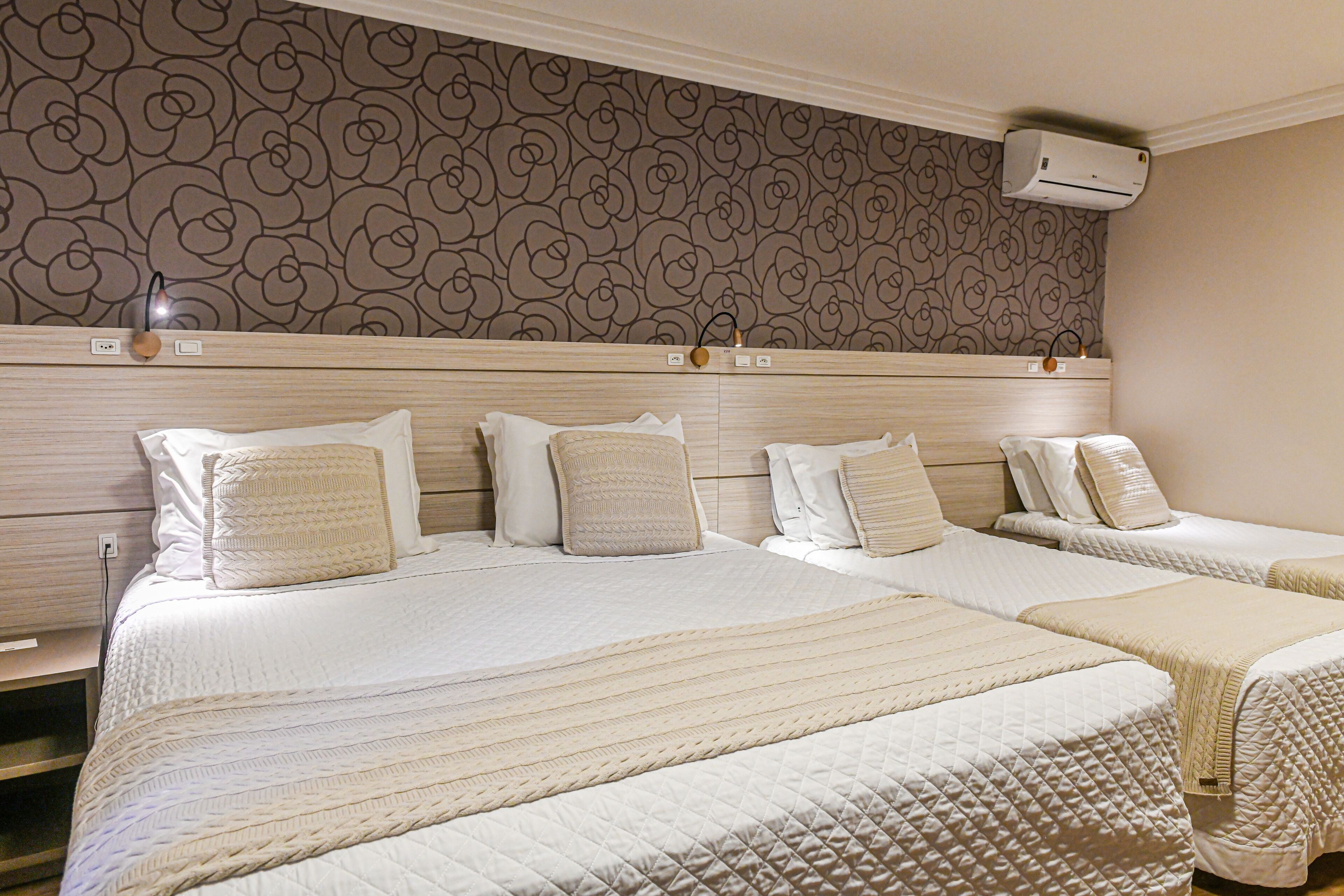 Habitación de hotel con dos camas, un papel tapiz estampado y un equipo de aire acondicionado.