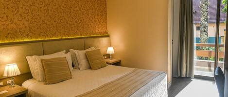 A hotel room with a large bed, two bedside lamps, a patterned wallpaper, and a view of the outside through a sliding door.