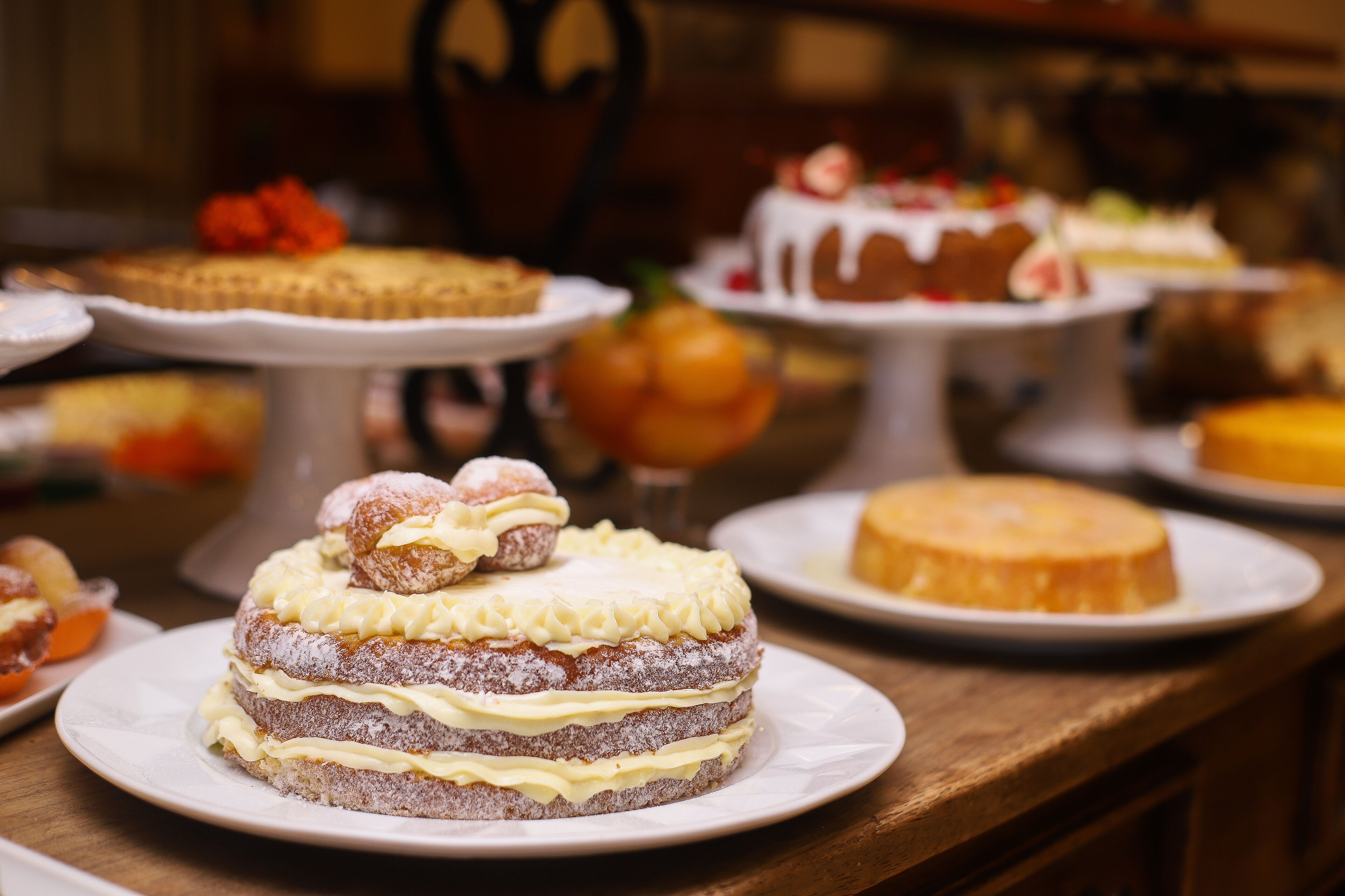 Verschiedene Kuchen sind ausgestellt, darunter ein mehrschichtiger Kuchen mit Sahne und ein Kuchen mit weißem Zuckerguss.