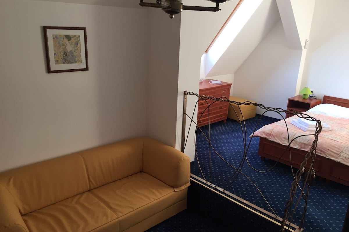 Ein Zimmer mit einem braunen Sofa, einem Bett mit blumigem, blauem Bettbezug, einer Holzkommode und einem gerahmten Bild an der Wand.