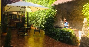 Un patio al aire libre con piso de ladrillo, una mesa con sillas y un paraguas grande.