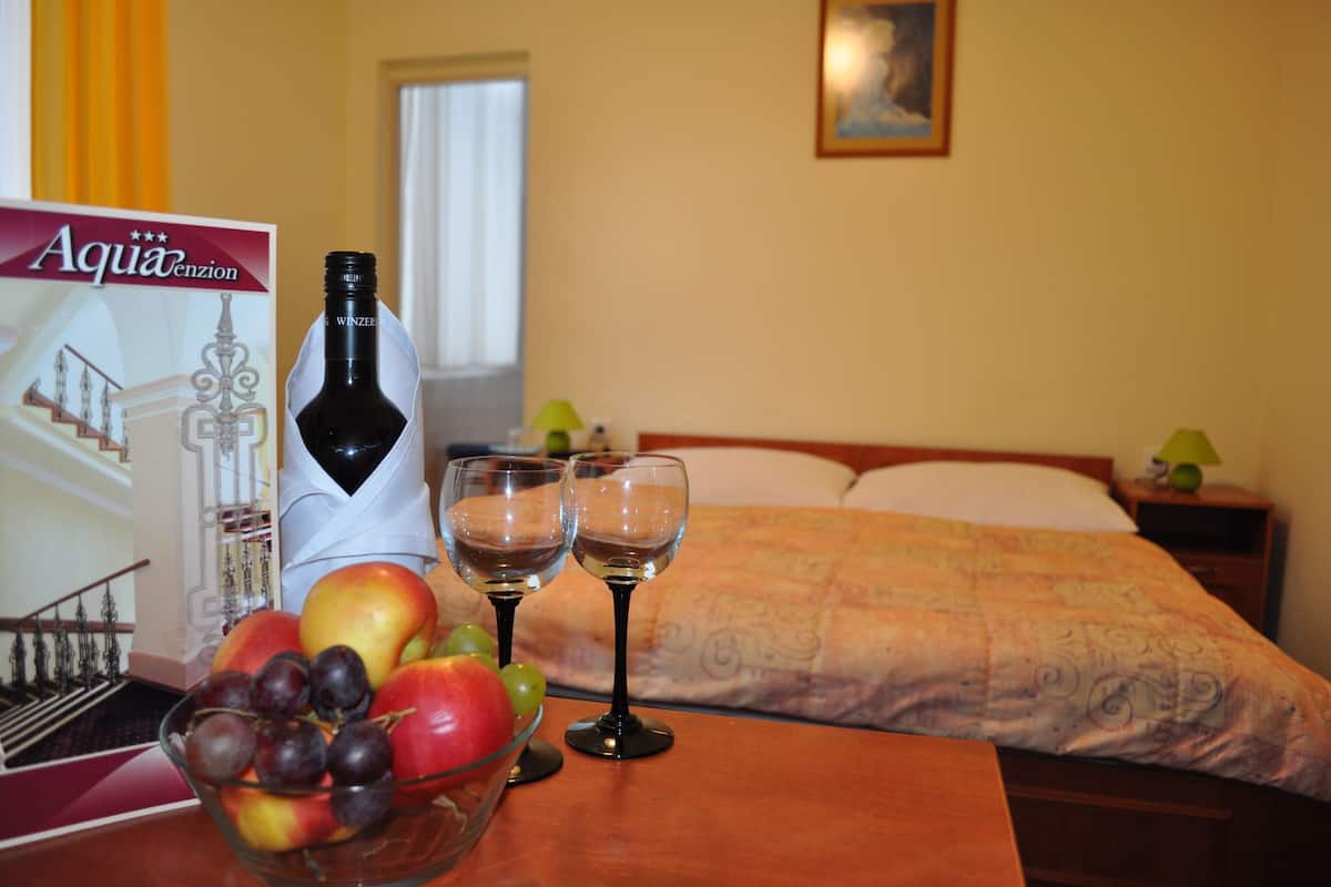 Ein Hotelzimmer mit einem Bett, einem Nachttisch mit Lampe, einem Tisch mit einer Weinflasche und Gläsern sowie einer Obstschale.