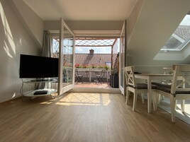 Una habitación moderna con televisión, suelo de madera, balcón con mesa y sillas, y tragaluz.