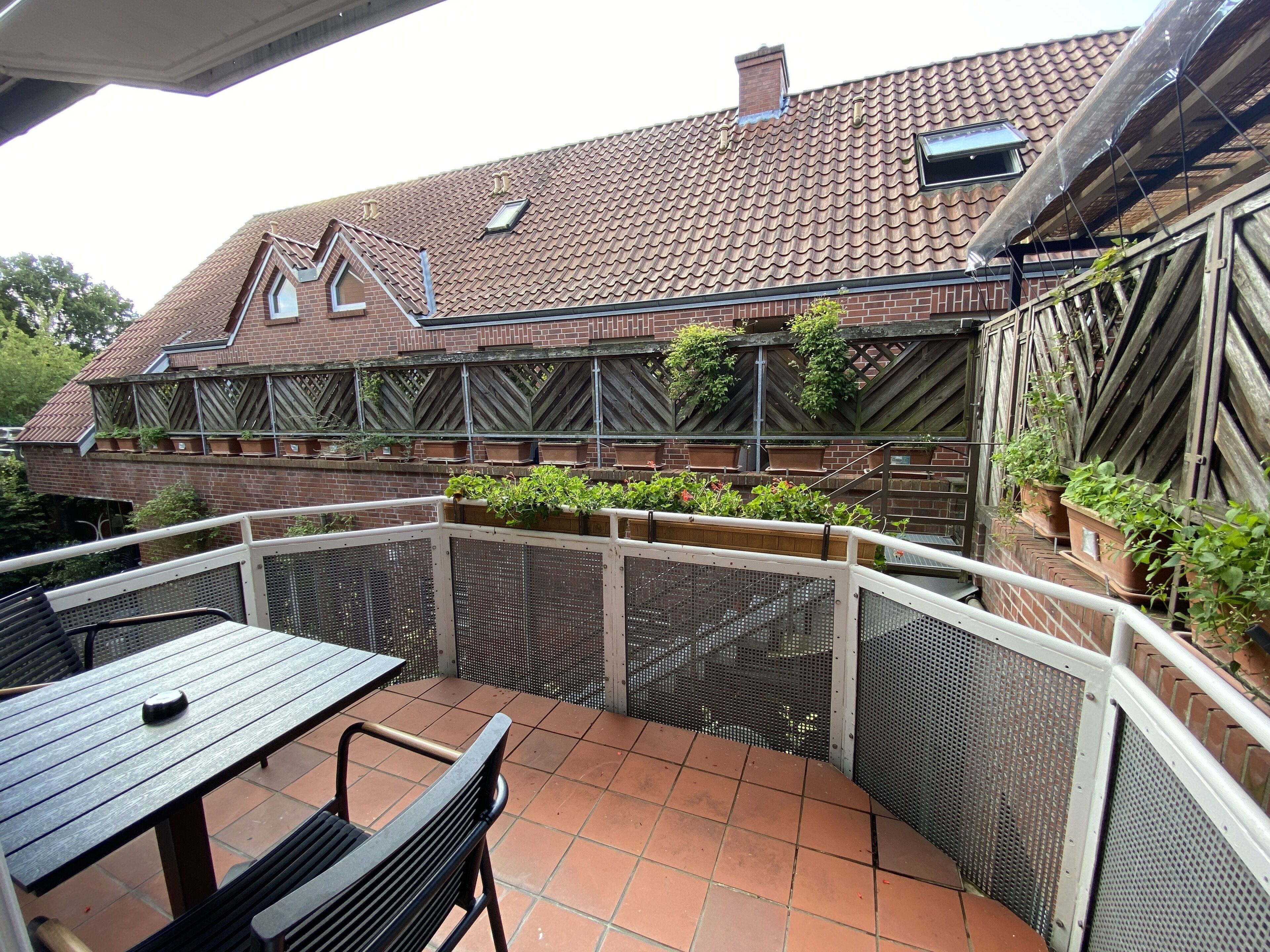 Un patio con mesa y sillas, un muro de ladrillo y una pérgola de madera, y un tejado de tejas.