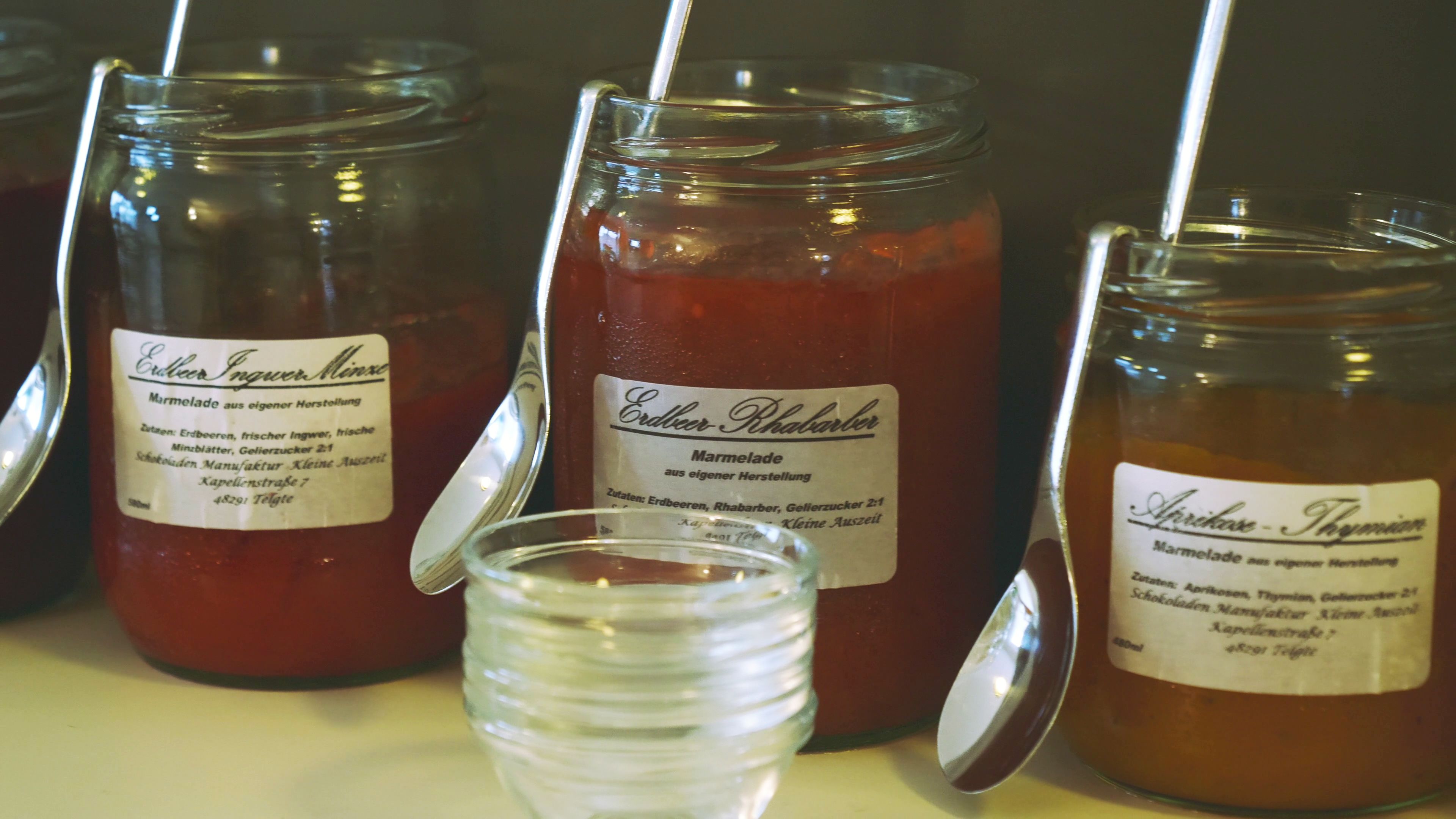 Three glass jars with labels, one of which is open, and a clear plastic cup with a spoon.