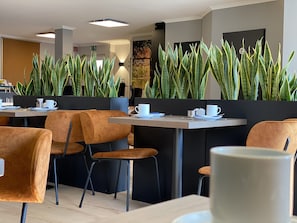 A modern cafe with orange chairs, tables, and green plants. - Hotel zur Bever (Telgte)