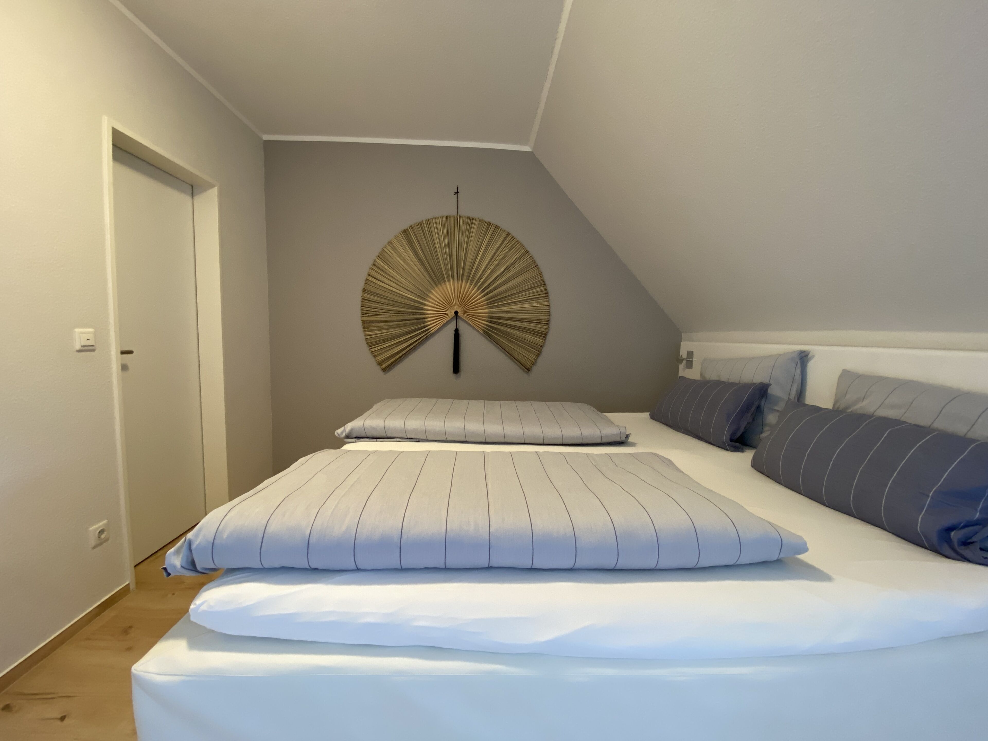 A bedroom with a bed, pillows, a wall-mounted fan, and a door.