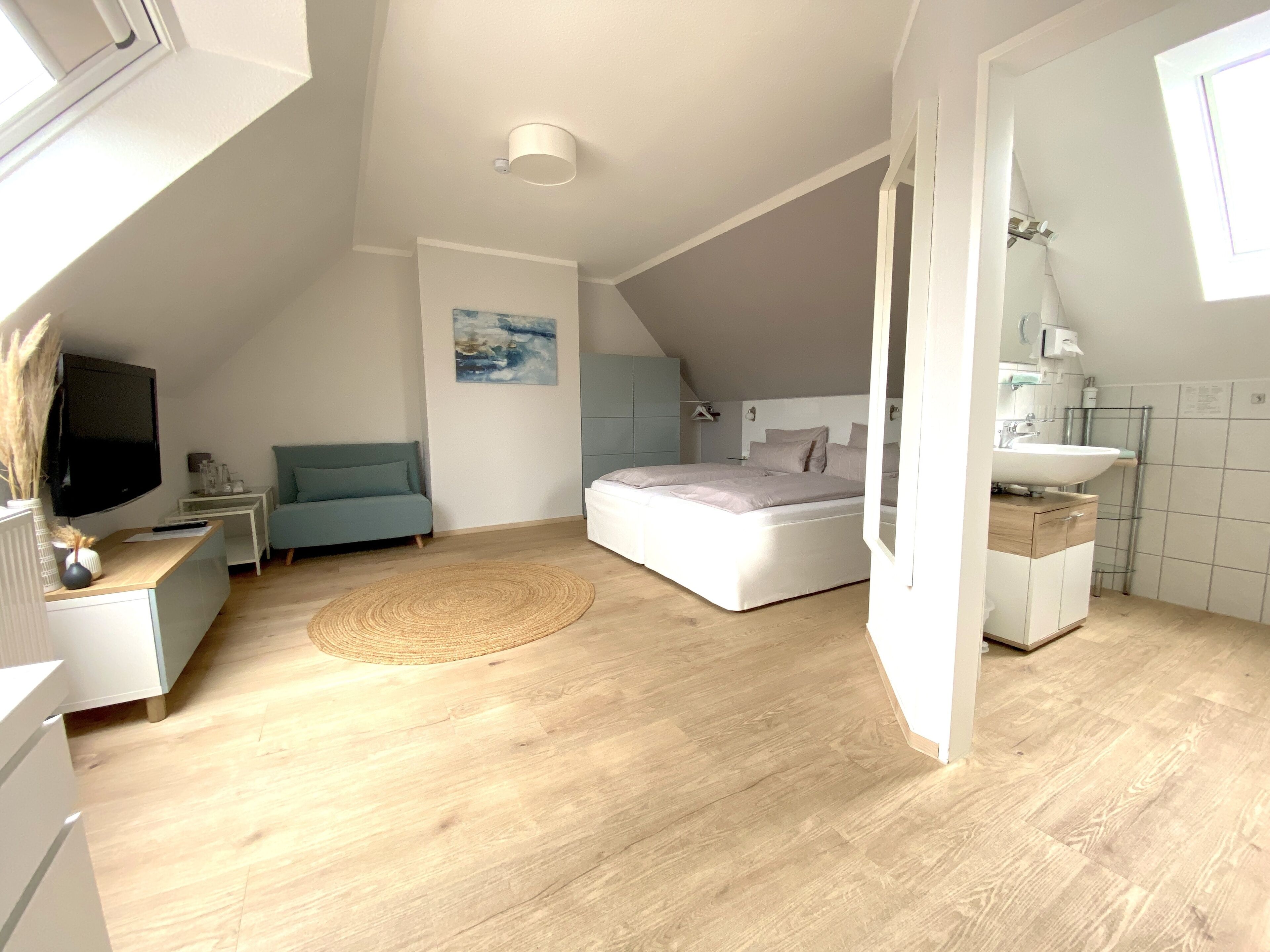 A modern bedroom with a bed, a sofa, a TV, and a bathroom.