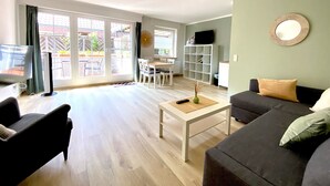A living room with a sofa, a coffee table, a TV, and a dining area with chairs and a table. - Hotel zur Bever (Telgte)
