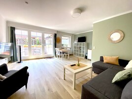 Una sala de estar con sofá, mesa de centro, televisor y un comedor con sillas y una mesa.