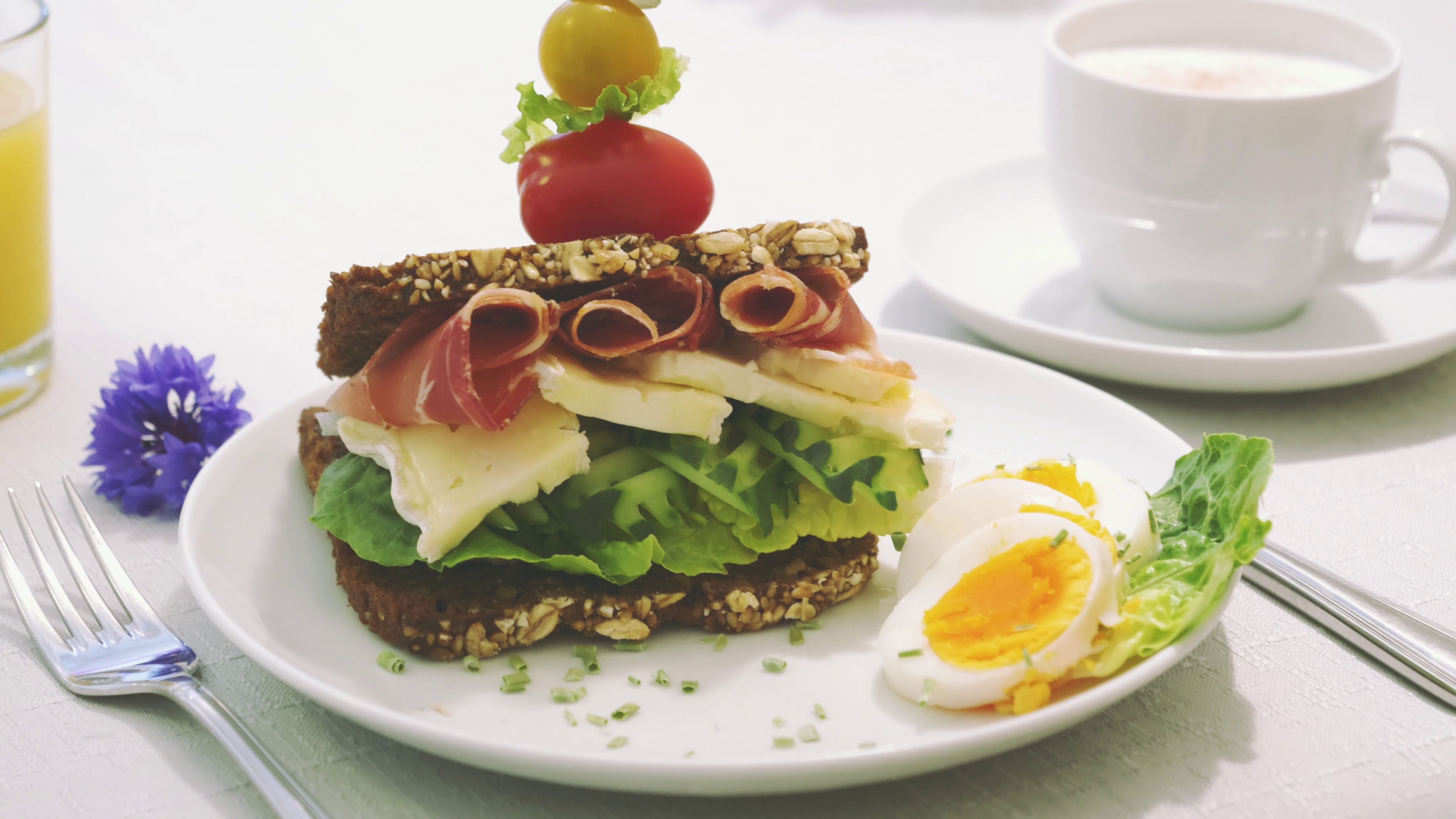 A sandwich on a plate with a fork and a cup of coffee nearby.