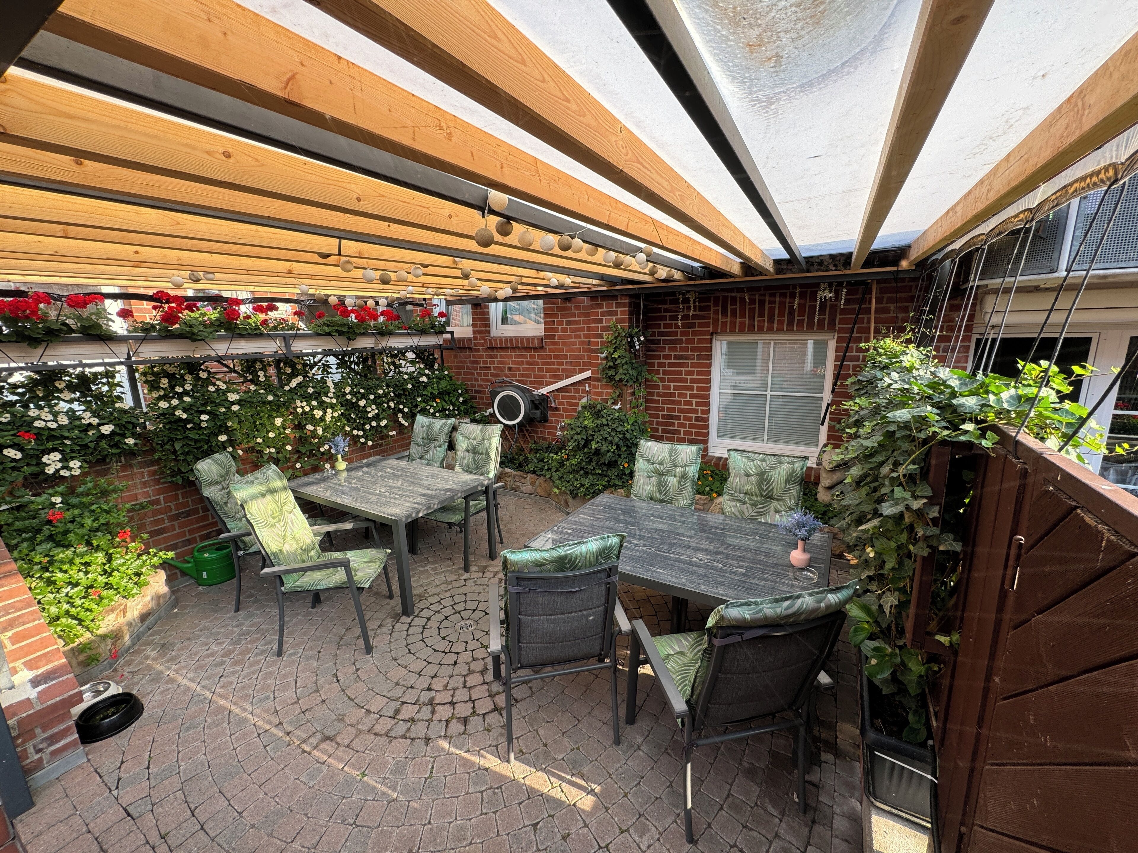 Un patio con una pérgola de madera, un muro de ladrillo y una mesa con sillas.