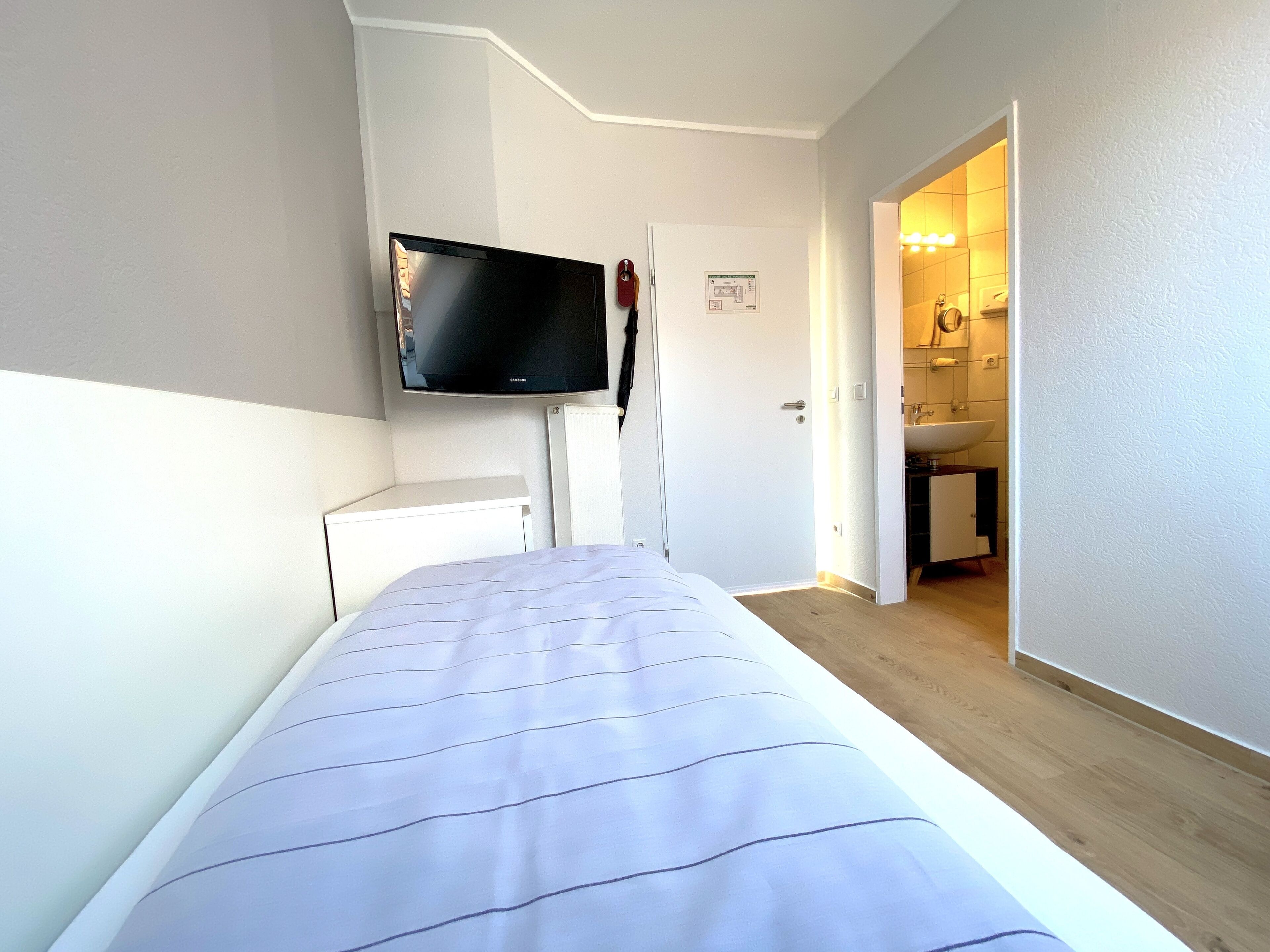 Un dormitorio con una cama, un televisor montado en la pared y una puerta que da a un baño.
