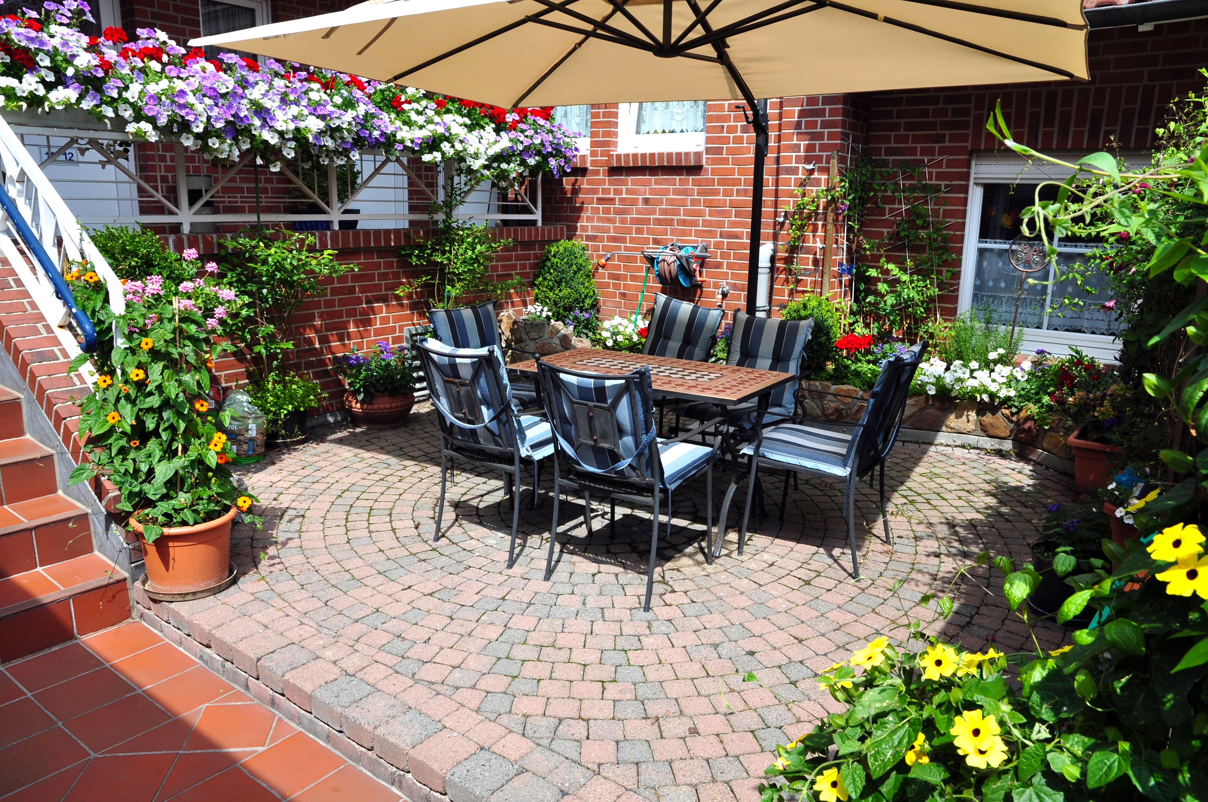 An outdoor patio with a brick floor, a table with chairs, and a large umbrella.