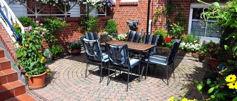 An outdoor patio with a brick floor, a table with chairs, and a large umbrella.