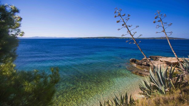 A coastal landscape with clear blue waters, rocky shore, and sparse vegetation. - Cast Away - Eco Village (Jelsa)