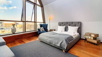 A modern bedroom with a large window, a bed, a chair, and a bedside table.