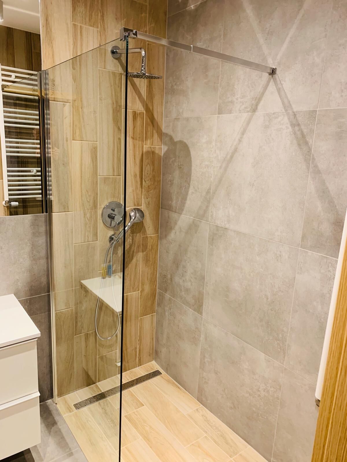 A modern shower enclosure with a glass door, a built-in shelf, and a handheld showerhead.