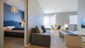 A modern living room with a sofa, a dining area with a table and chairs, and a kitchen area with a counter and appliances.