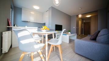 Una sala de estar moderna con un sofá gris, una mesa de comedor con sillas y una zona de cocina con armarios y un televisor.