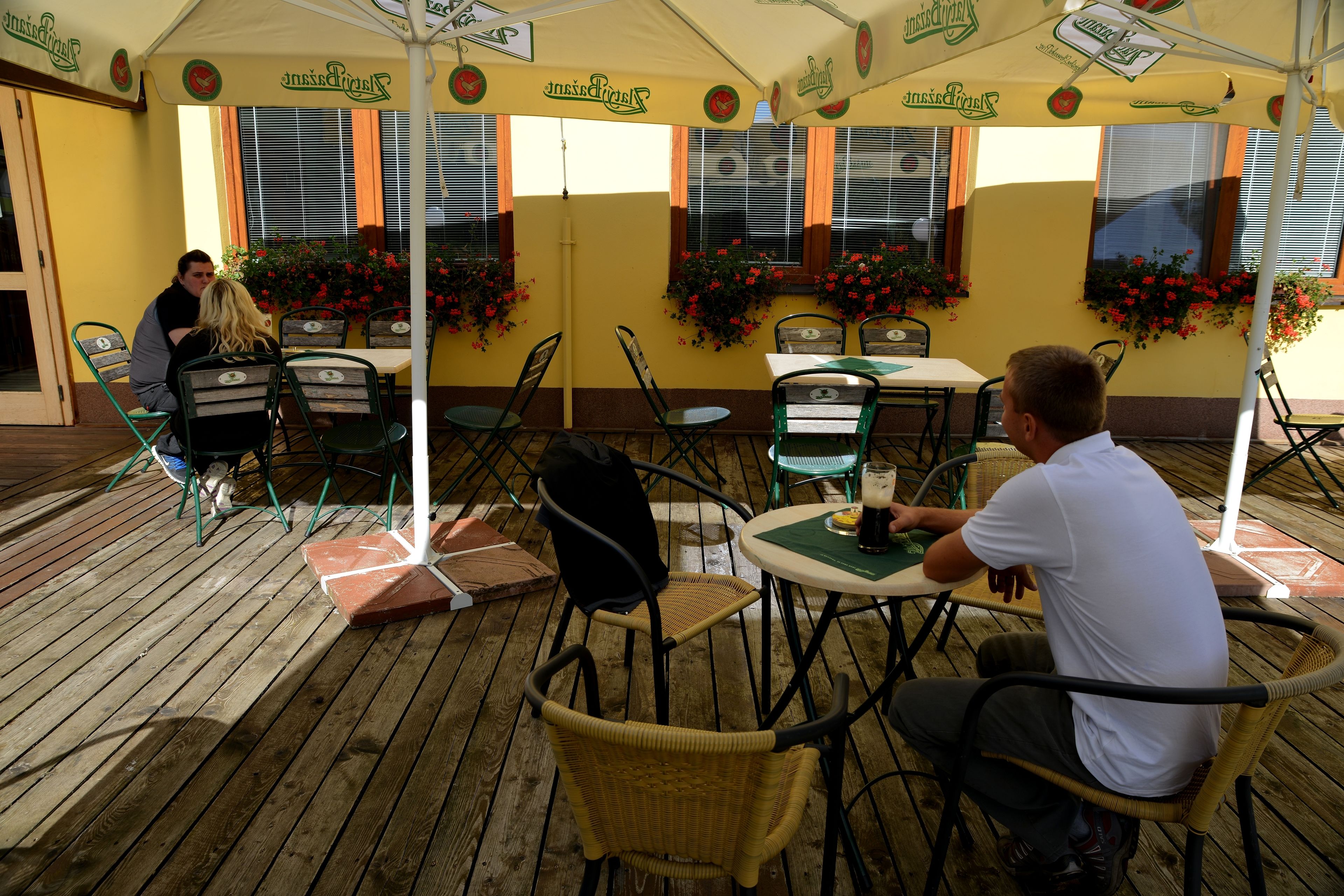 An outdoor seating area with tables and chairs under a canopy, surrounded by windows with flower boxes.