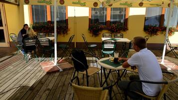 An outdoor seating area with tables and chairs under a canopy, surrounded by windows with flower boxes.