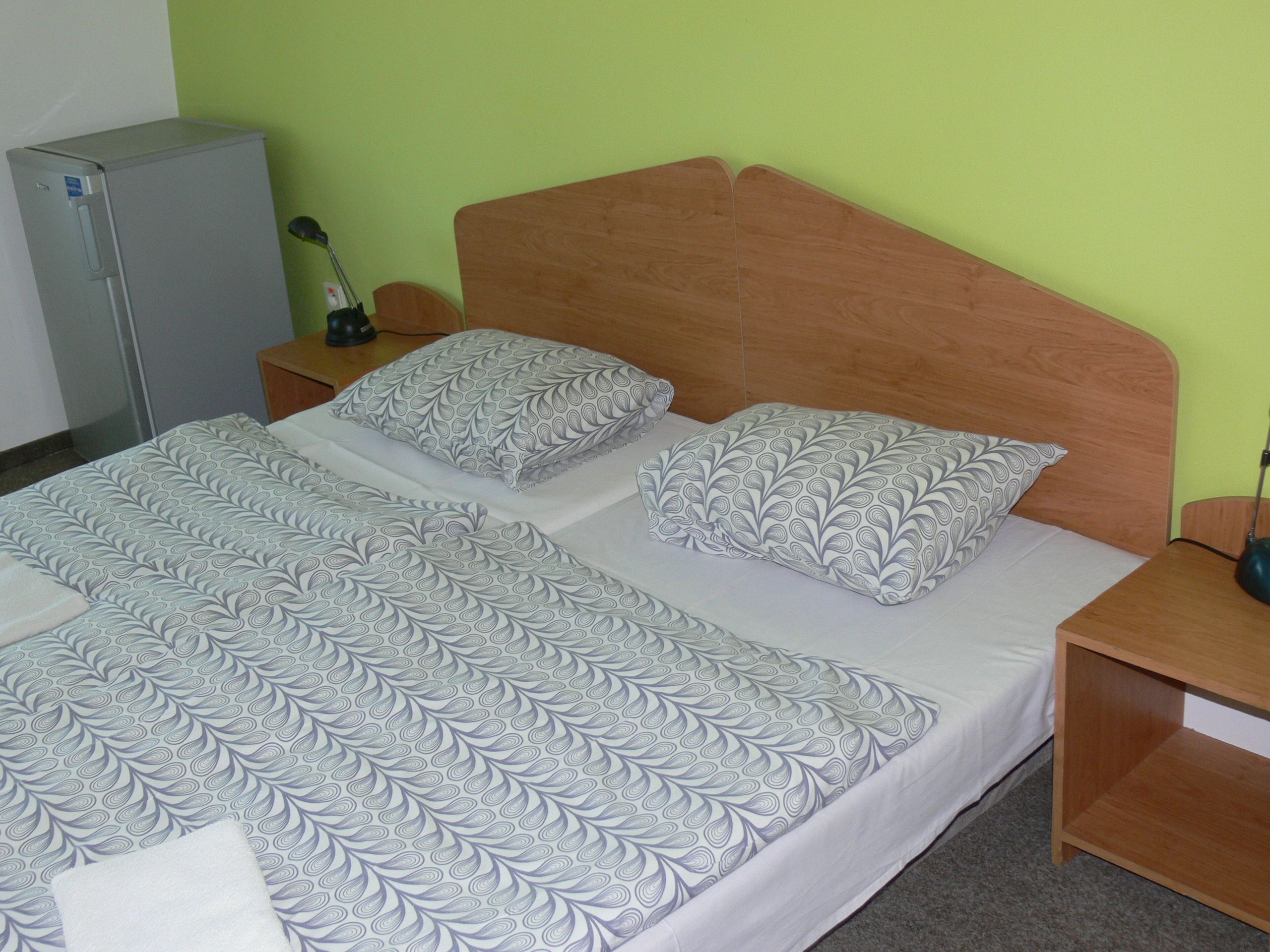 A neatly made bed with patterned bedding, a wooden headboard, and a small bedside table with a lamp.