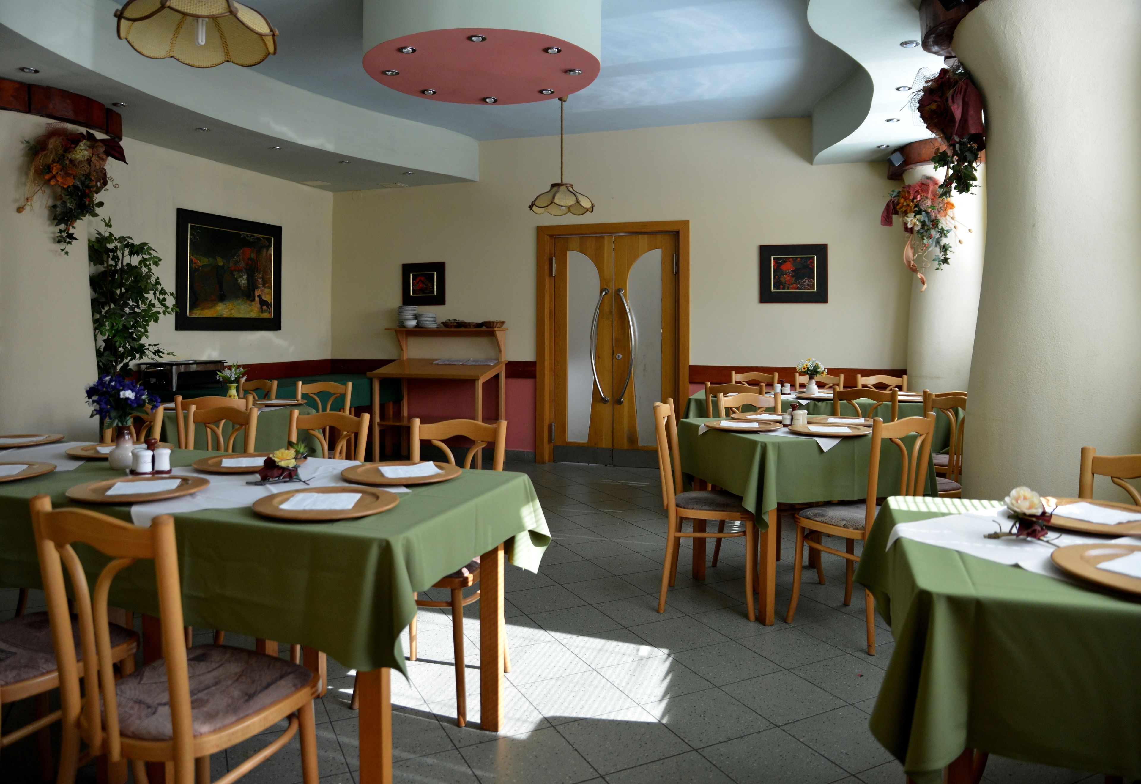 Un comedor con mesas dispuestas para comer, sillas de madera y una puerta de madera al fondo.