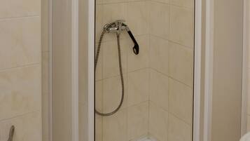 A corner shower with a glass door, a handheld showerhead, and a white base.