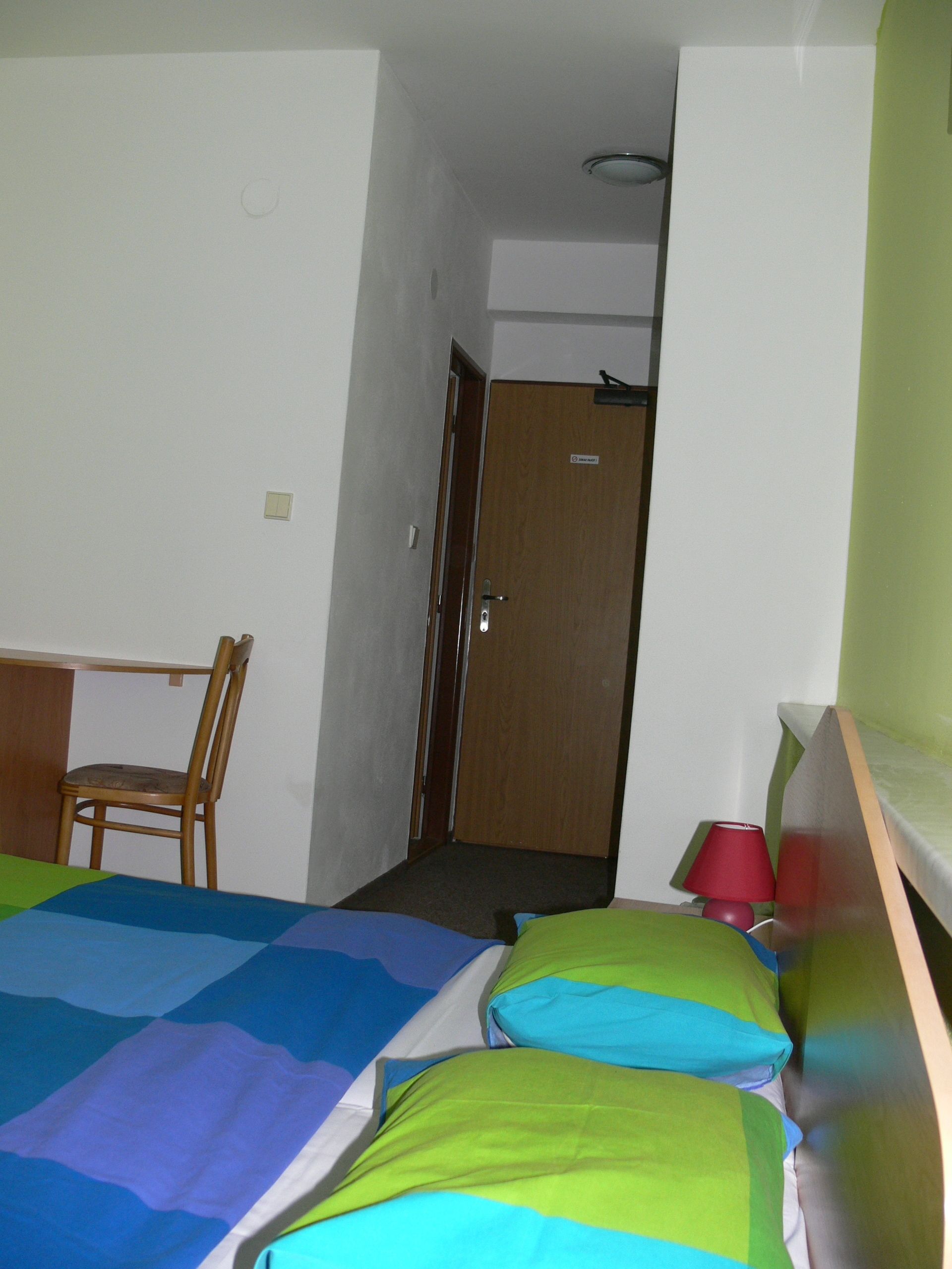 A small, simple room with a bed, a chair, and a desk.
