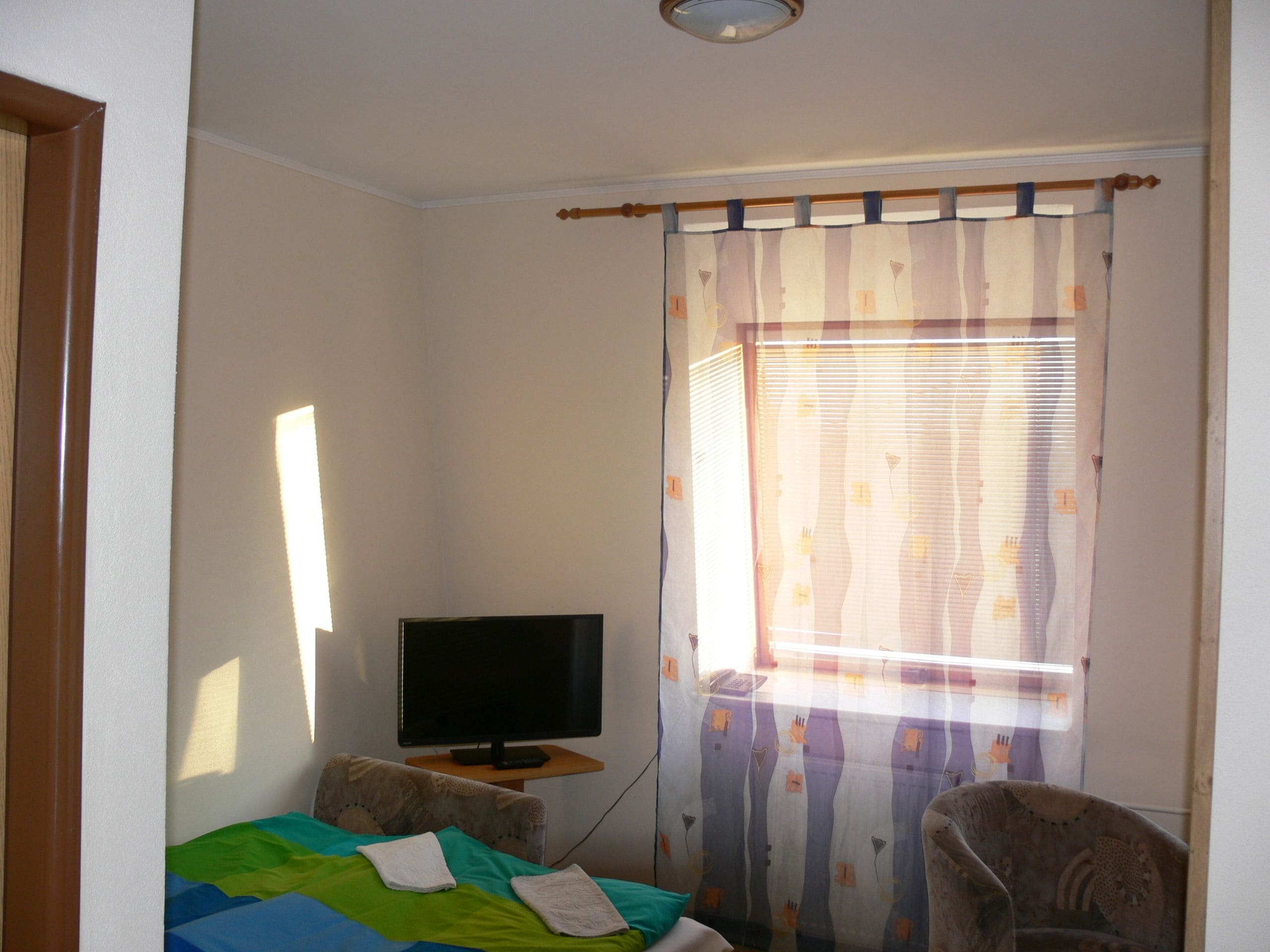 A bedroom with a bed, a chair, a television on a small table, and a window with curtains.