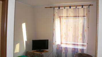 A bedroom with a bed, a chair, a television on a small table, and a window with curtains.