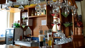 Zona de bar con varios vasos colgando del techo, un refrigerador y una barra con botellas y copas.