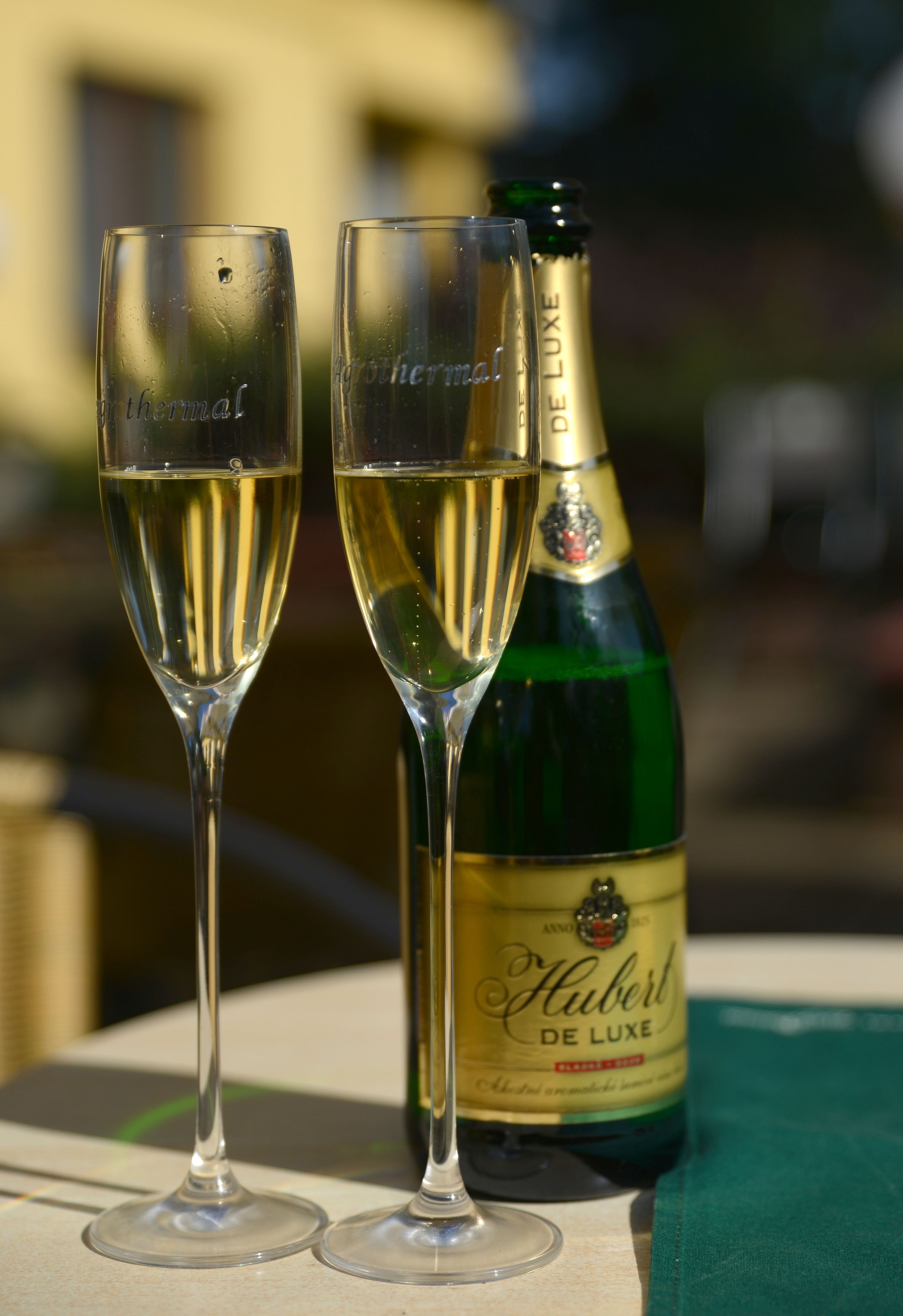 Dos copas de champán llenas de burbujas y una botella con la etiqueta 'Hubert De Luxe' sobre una mesa.