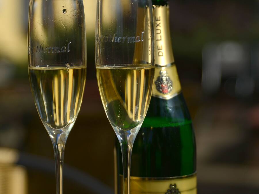 Dos copas de champán llenas de burbujas y una botella con la etiqueta 'Hubert De Luxe' sobre una mesa.