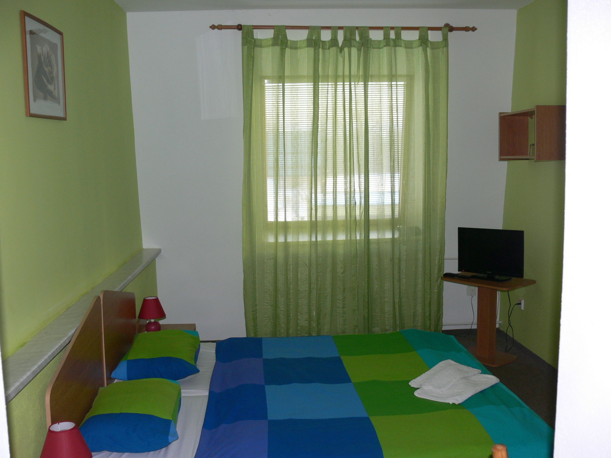 A room with a bed, a television, and a window with curtains.