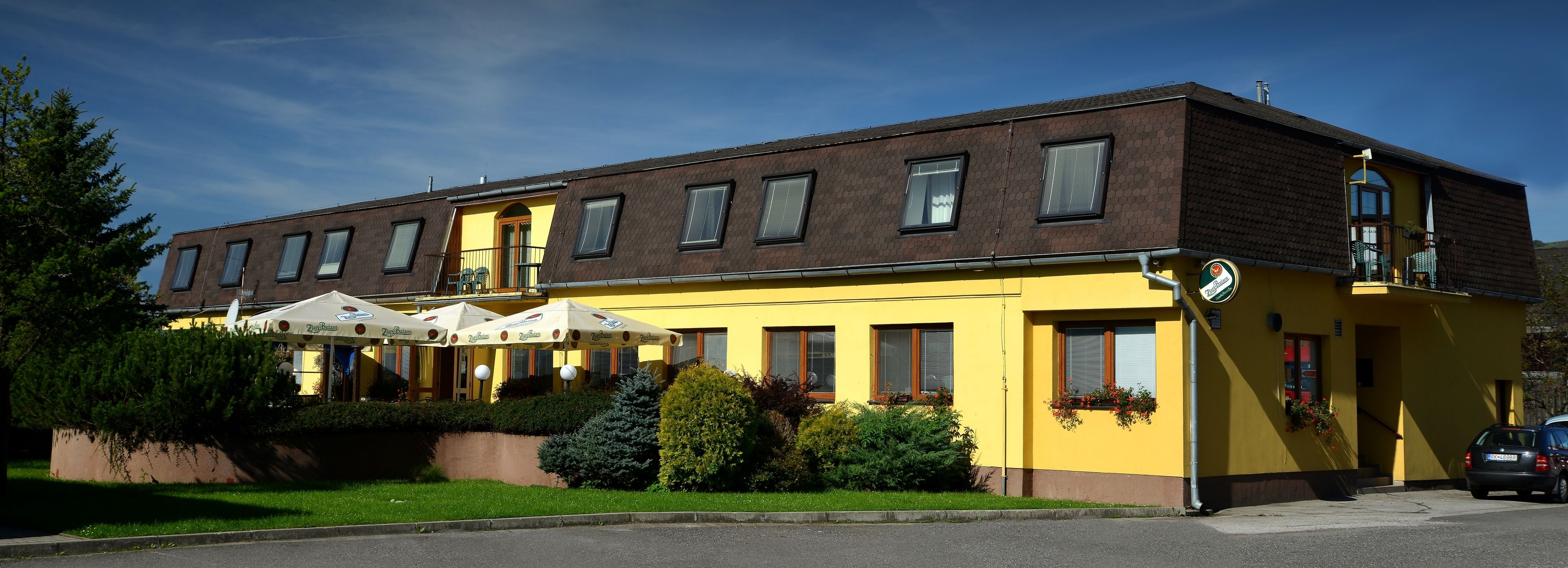 A yellow building with multiple windows and a balcony. There are outdoor umbrellas and a car parked nearby.