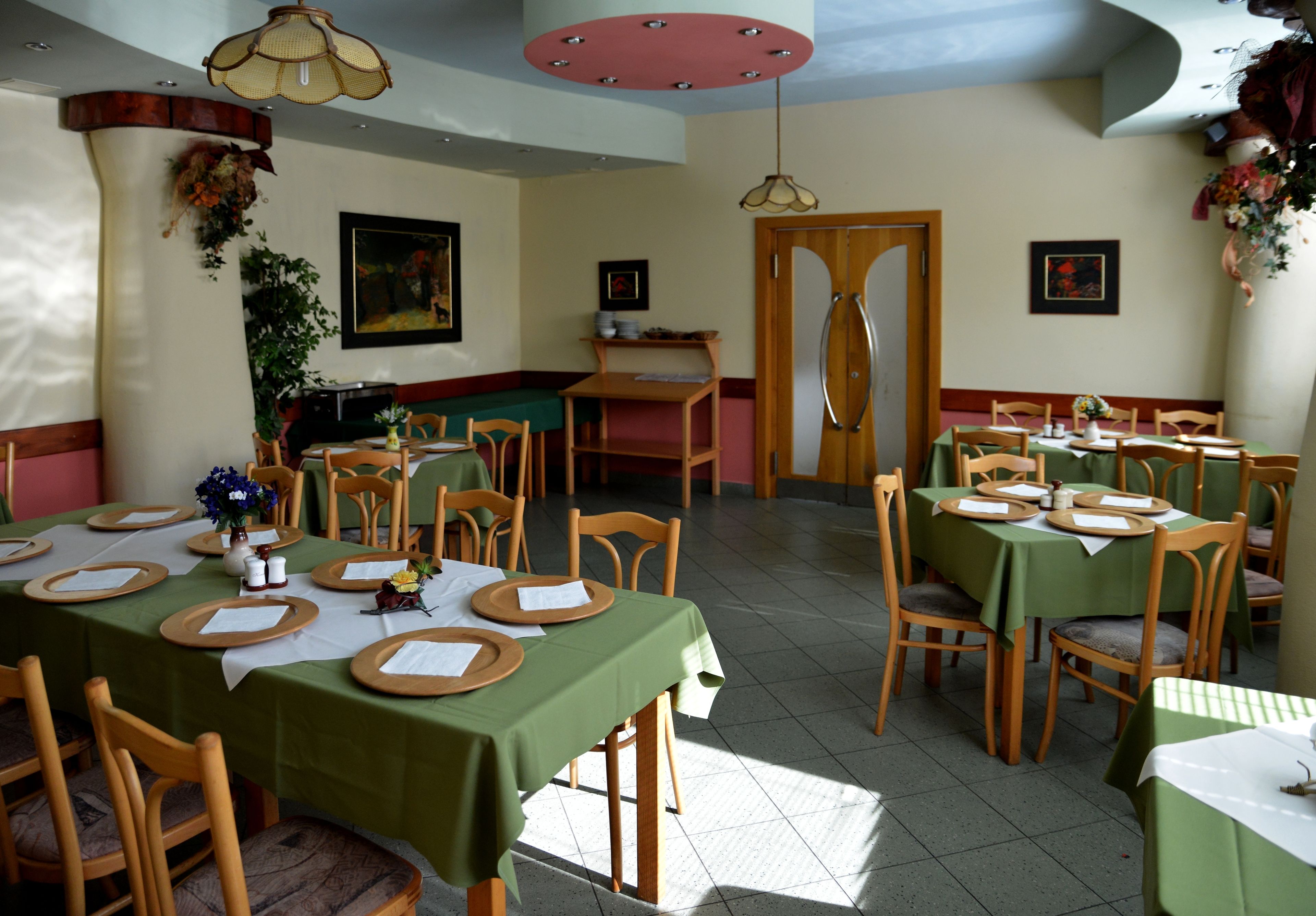 A dining area with multiple tables set for service, wooden chairs, and a kitchen area in the background.