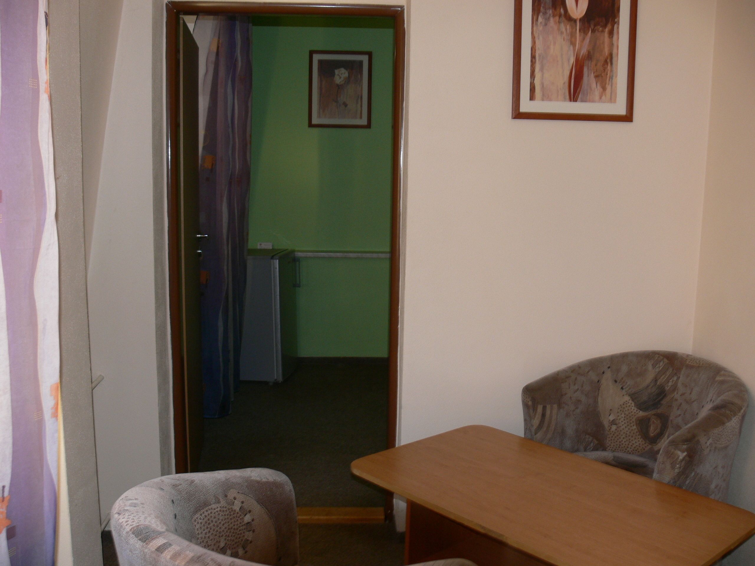 A room with a wooden table and two patterned chairs, a green wall, and a framed picture.