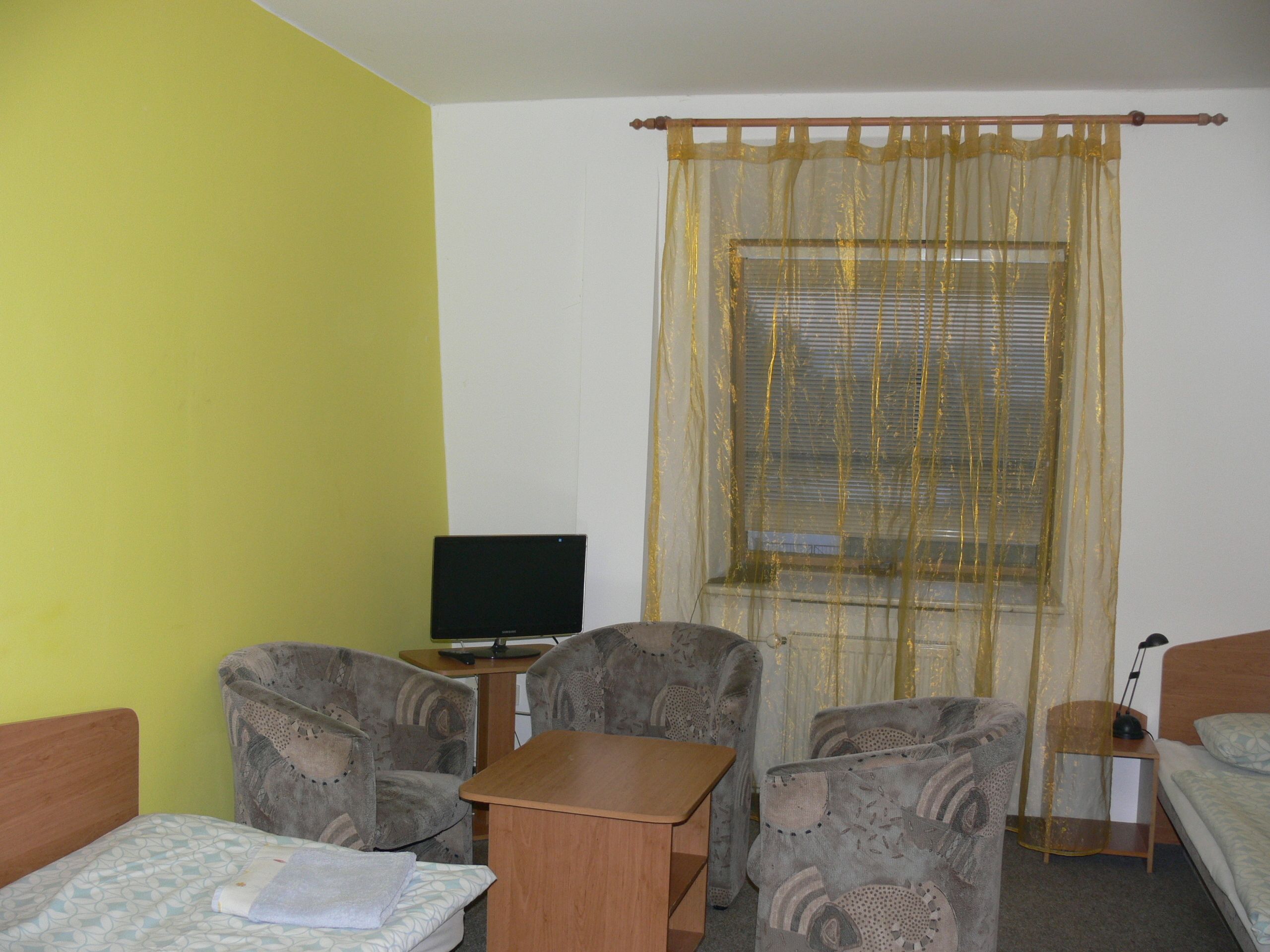 Una habitación con cama, dos sillones, una mesita, televisión y ventana con persianas.