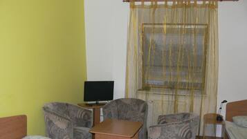 Una habitación con cama, dos sillones, una mesita, televisión y ventana con persianas.